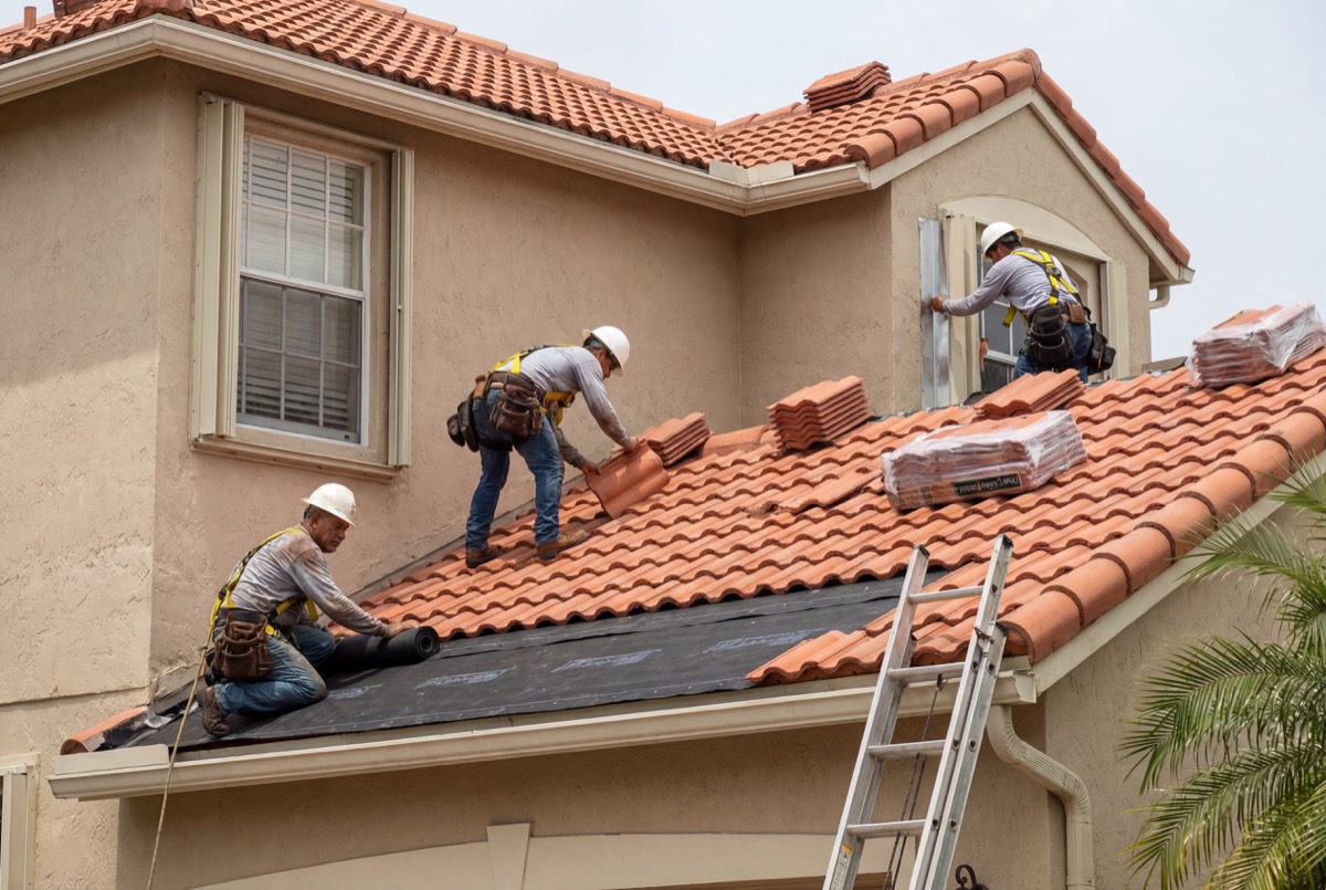Roofers installing clay tiles on house roof