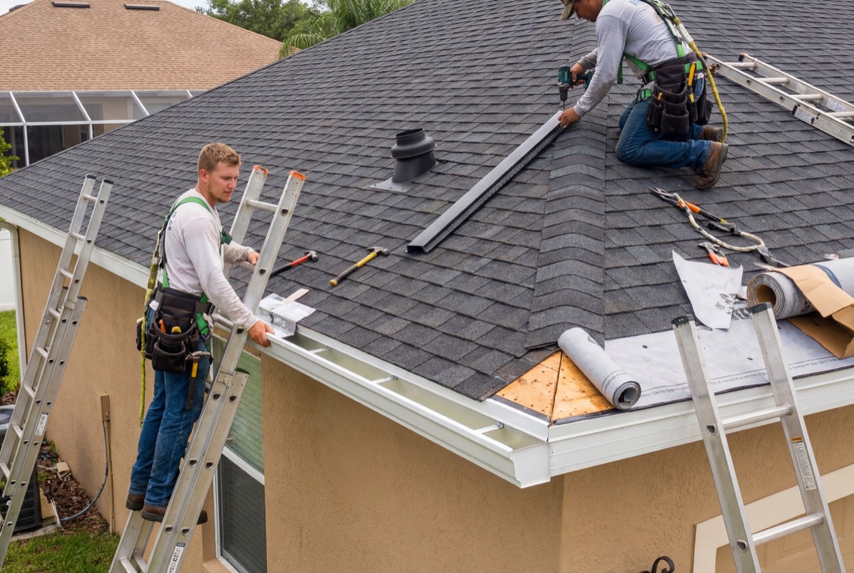 Roofers installing shingles on house roof
