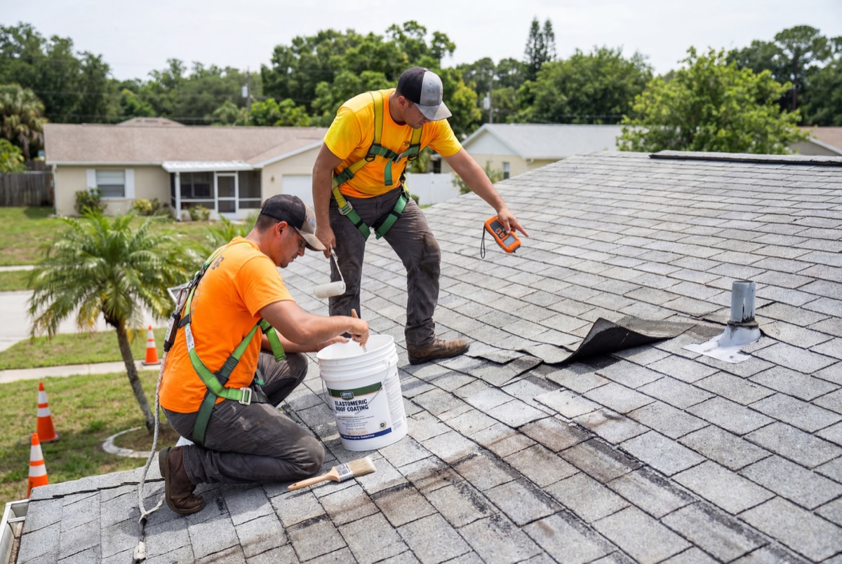 Roofers repairing asphalt shingles on house roof