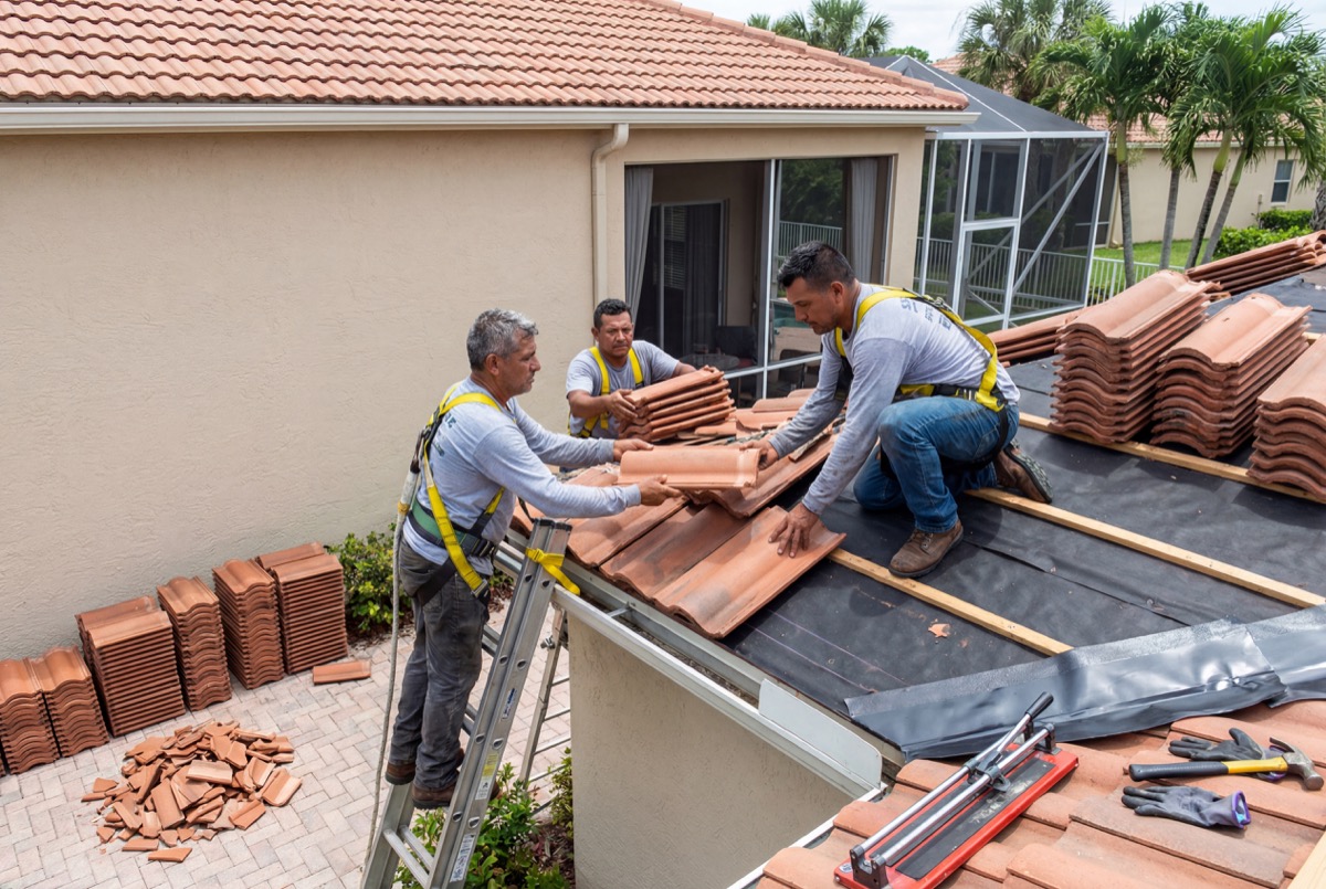 Roofers installing clay tiles on house roof