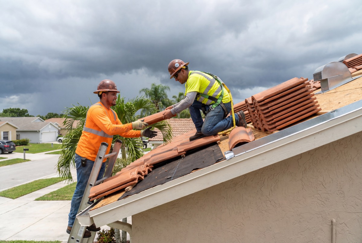 Roofers installing clay tiles on house roof