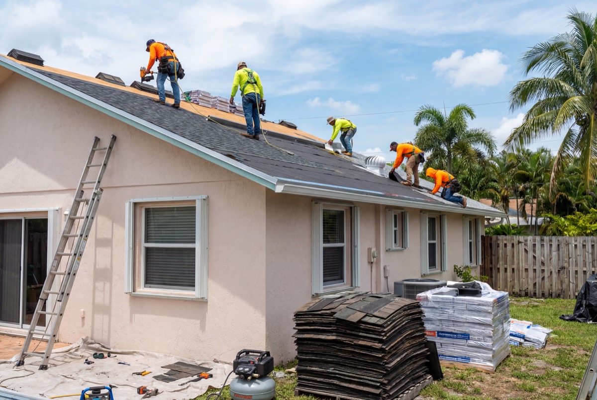 Workers installing shingles on house roof